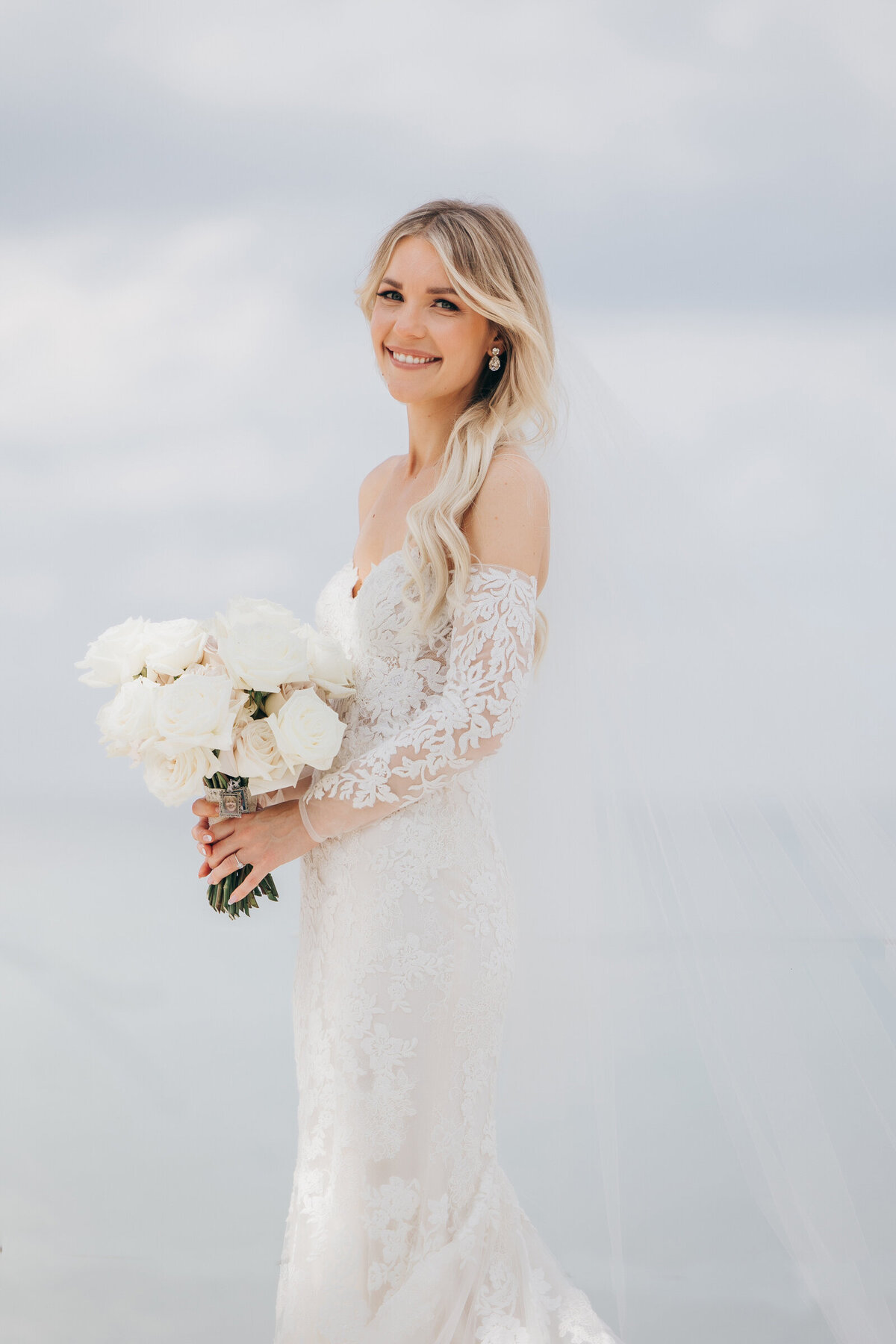 Elegant bridal portraits of bride wearing luxurious lace dress while holding chic white roses