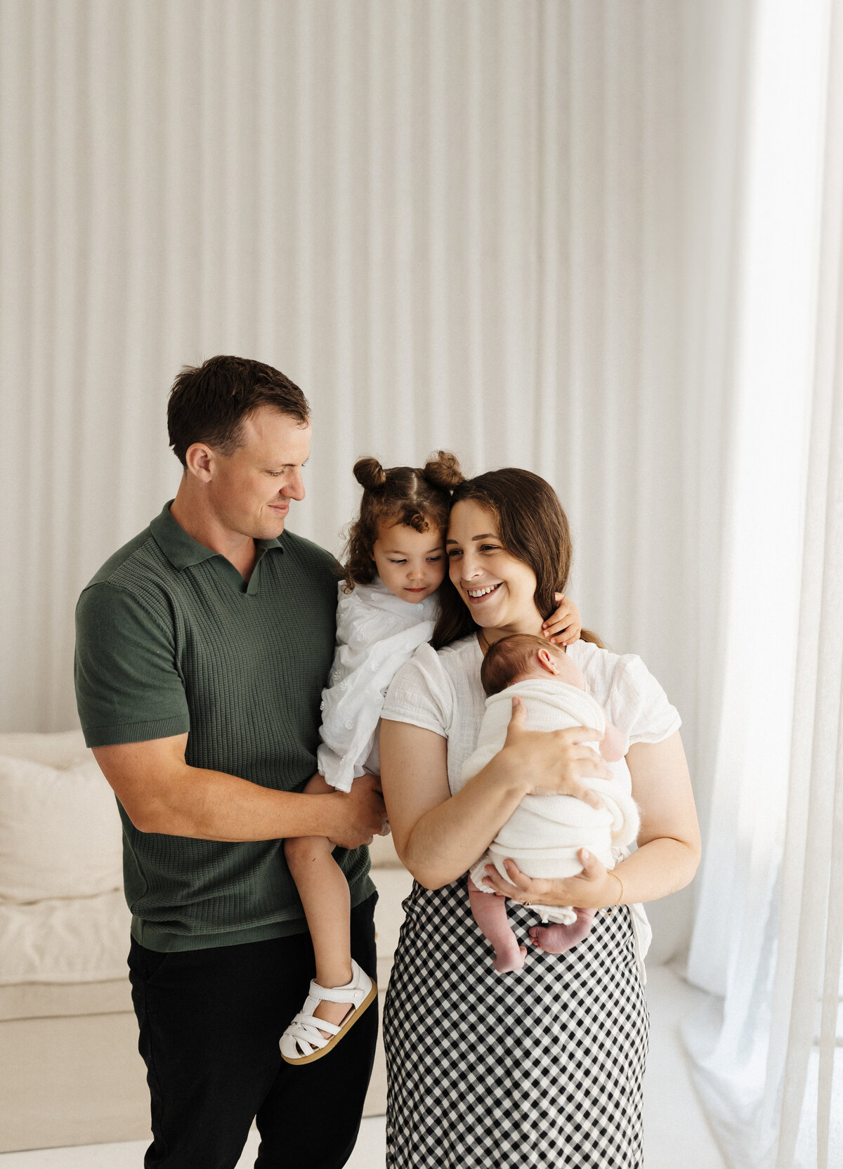 A mother and father holding their newborn child and little girl in a Christchurch photography studio specializing in newborns