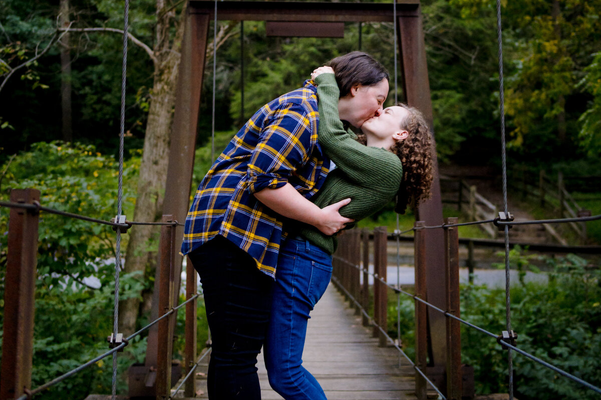 A couple kissing as they lean back and stand on a small bridge.