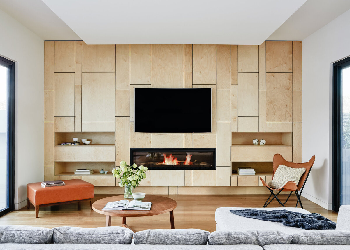 A flatscreen tv is hung on a wooden feature wall in a modern living room with a sleek fireplace inset.