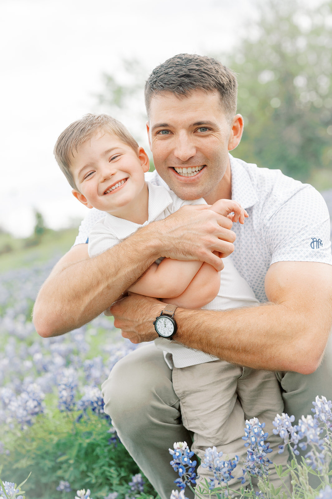 Father and son playing in a grassy field surrounded by bluebonnets