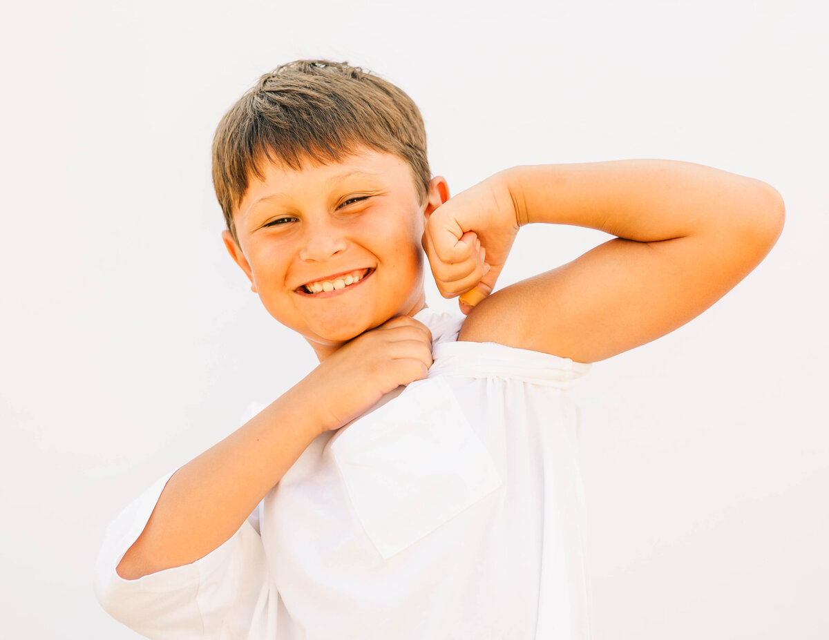 Boy in 5th grade flexing his muscles against clean white backdrop