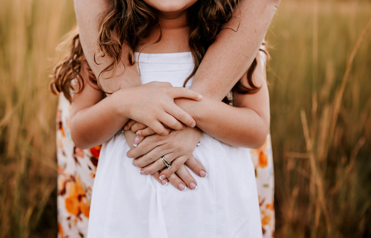 Close up of mom hugging her daughter from behind ad their hands overlapping