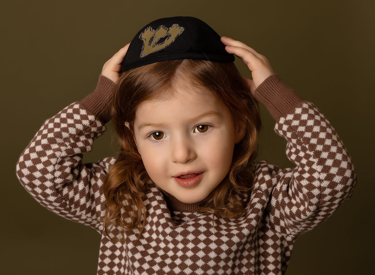 Little boy's portrait is captured in brooklyn, ny to commemorate his upsherin. He is holding a kippah on his head. Captured by brooklyn family photographer Chaya Bornstein.