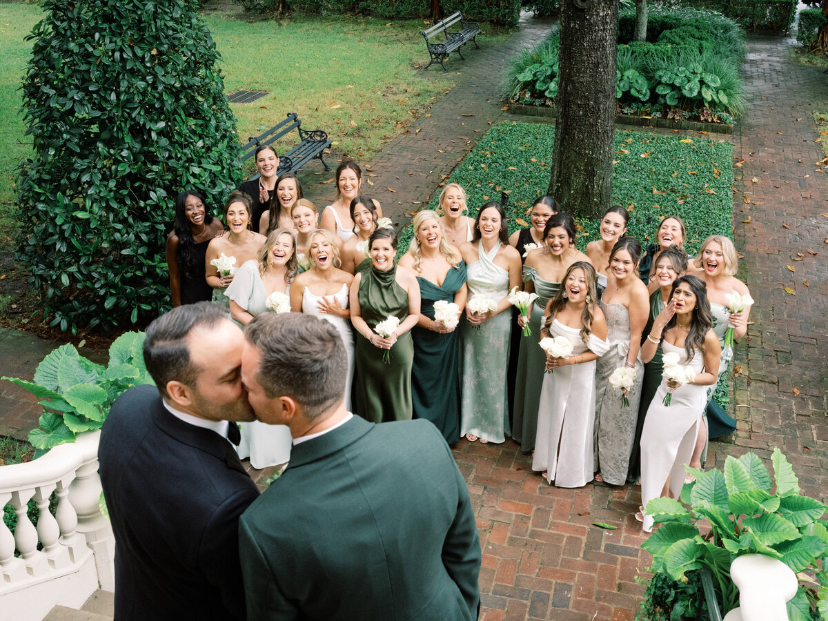 A touching moment as a couple kisses passionately while surrounded by their joyful wedding guests, highlighting the community of love and support during their celebration.