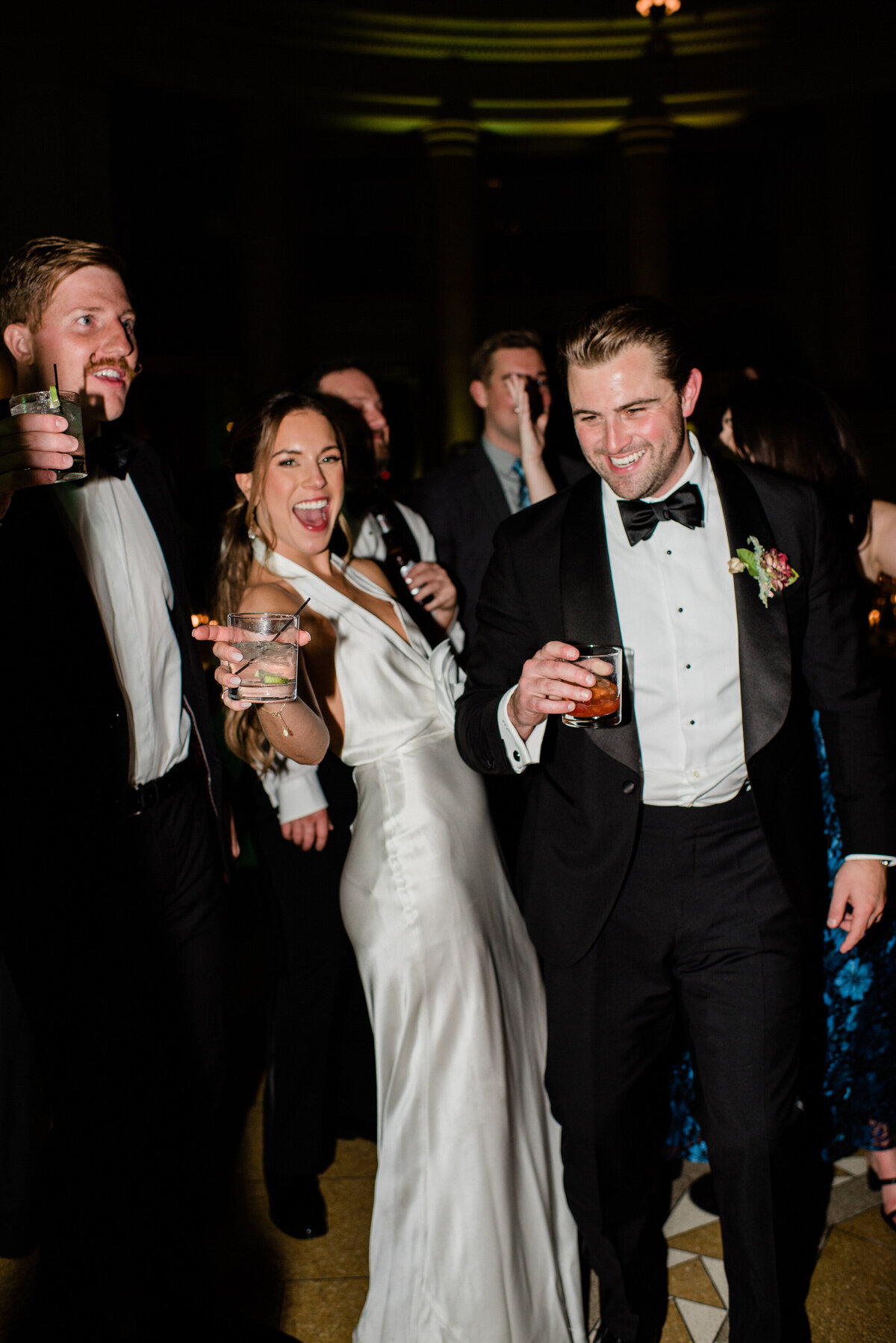 Bride and two groomsmen pose with drinks in hand 