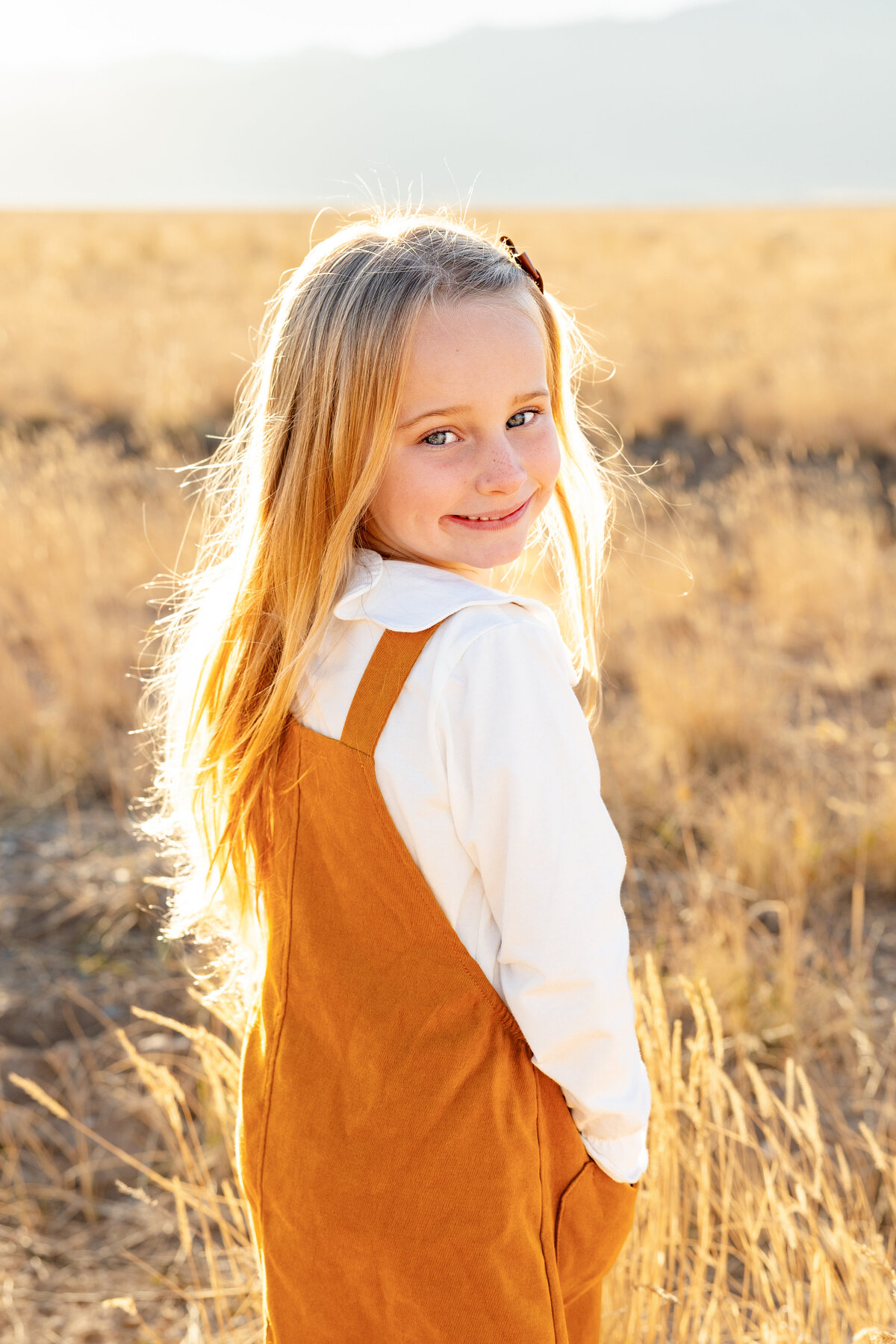A young girl glances over her shoulder with a playful smile, her golden hair glowing in the evening light.