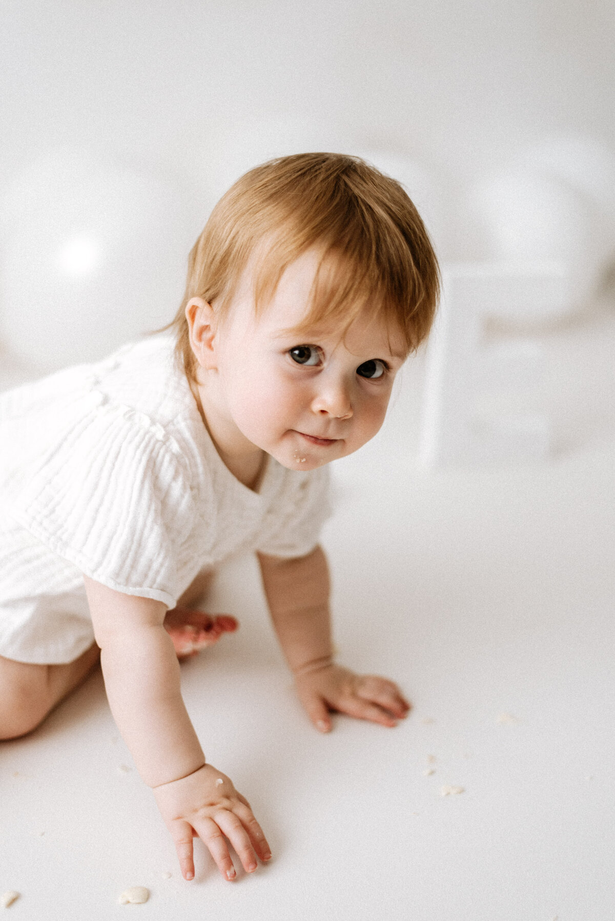 Baby girl crawling and smiling on white floor at Billingshurst cake smash photoshoot