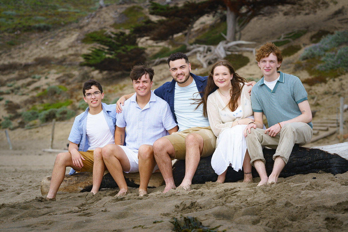 family of five kids sitting on a log at the beach posing for photos