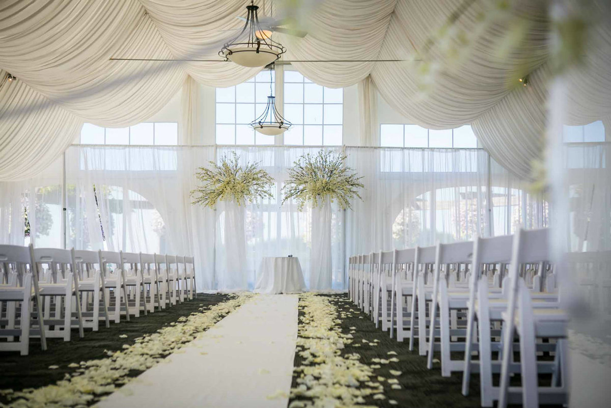 wedding ceremony in large tent with large orchid wedding arch and aisle lined on white rose petals