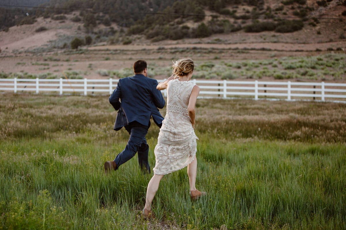 A couple runs in a field towards a fence.