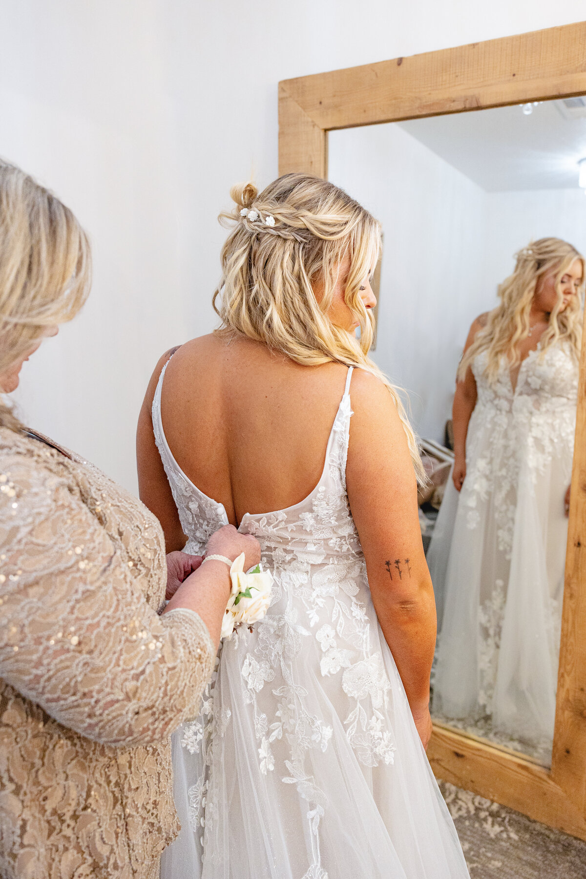 A touching moment as the bride's mother  fastens the back of the bride’s lace wedding gown. The bride, seen in the mirror’s reflection, looks serene and radiant.