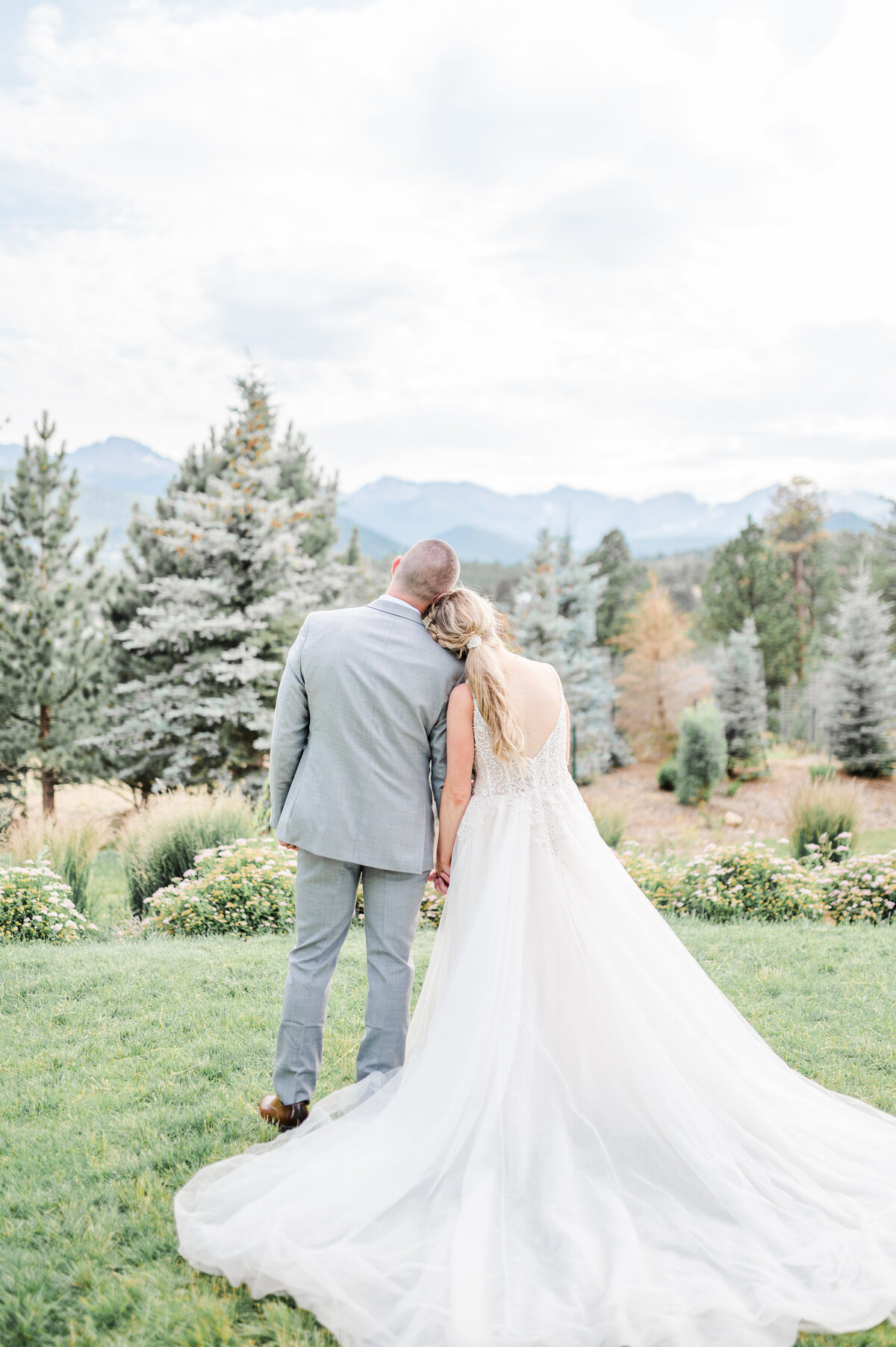 couple holding hands and looking at the mountains on a grassy lawn at the stanley hotel