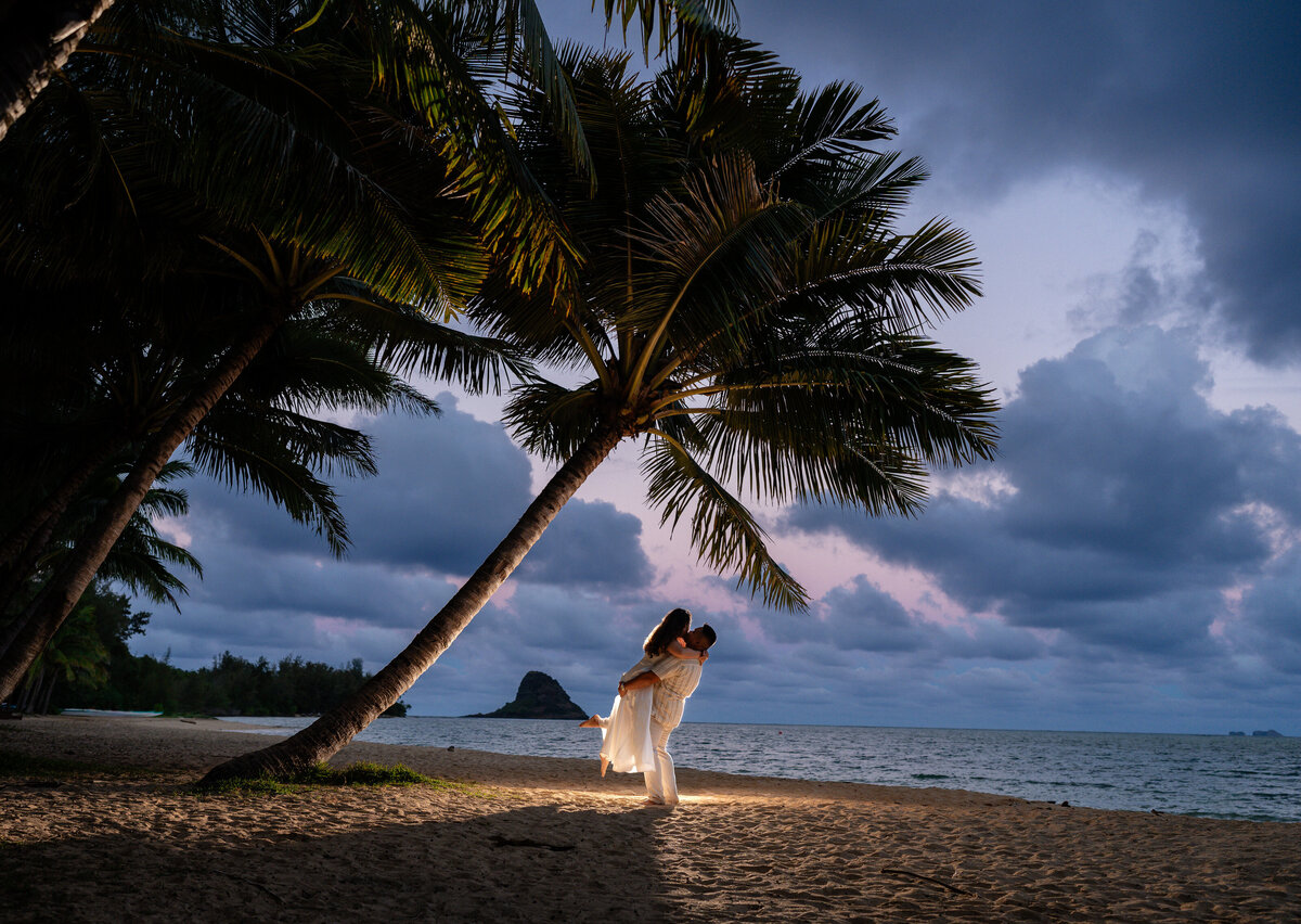 Oahu Hawaii Elopement Adventurous Asian couple at Secret Island Beach during blue hour at night with off camera flash lift and kiss.