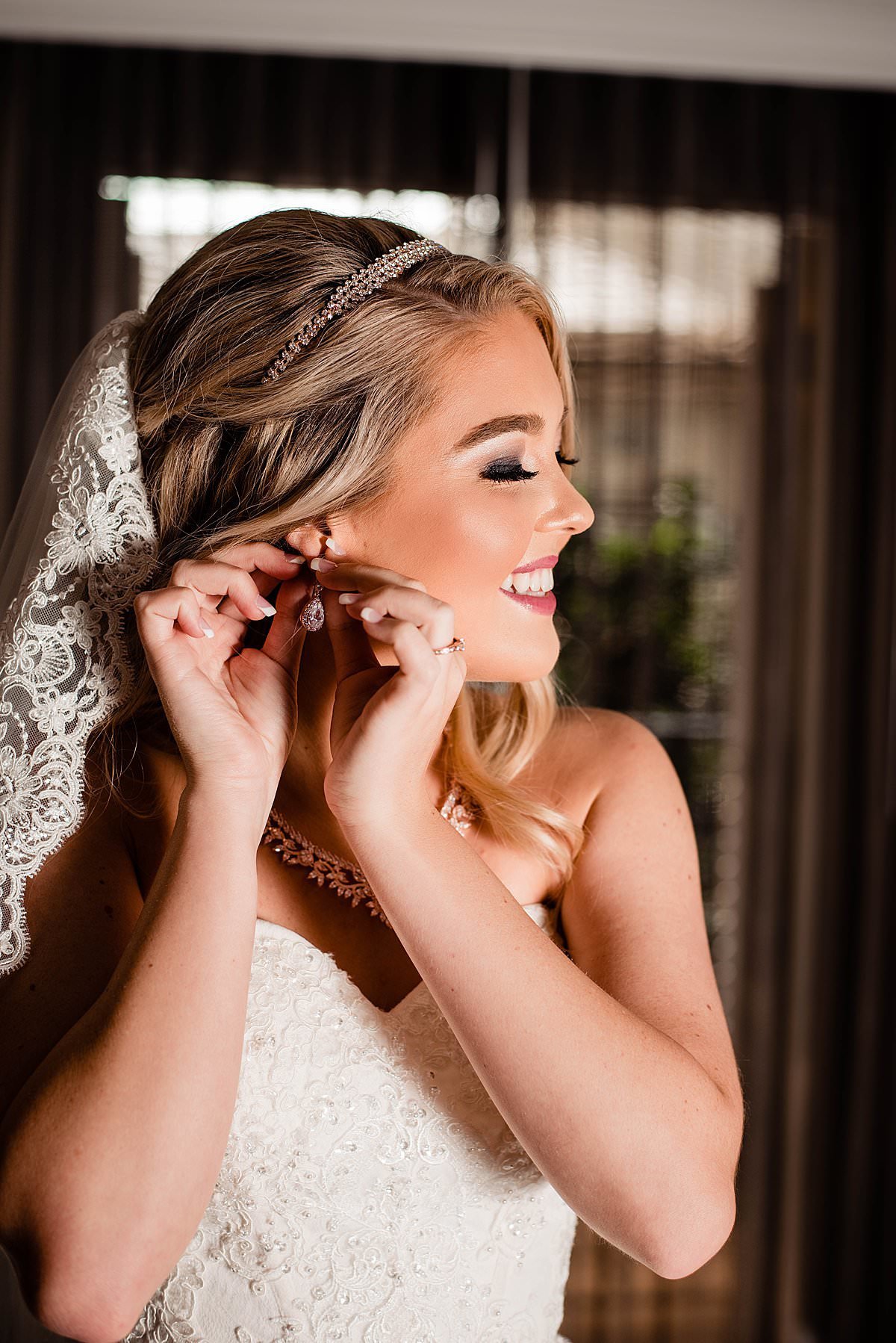 Bride smiling and putting her earrings in while getting ready