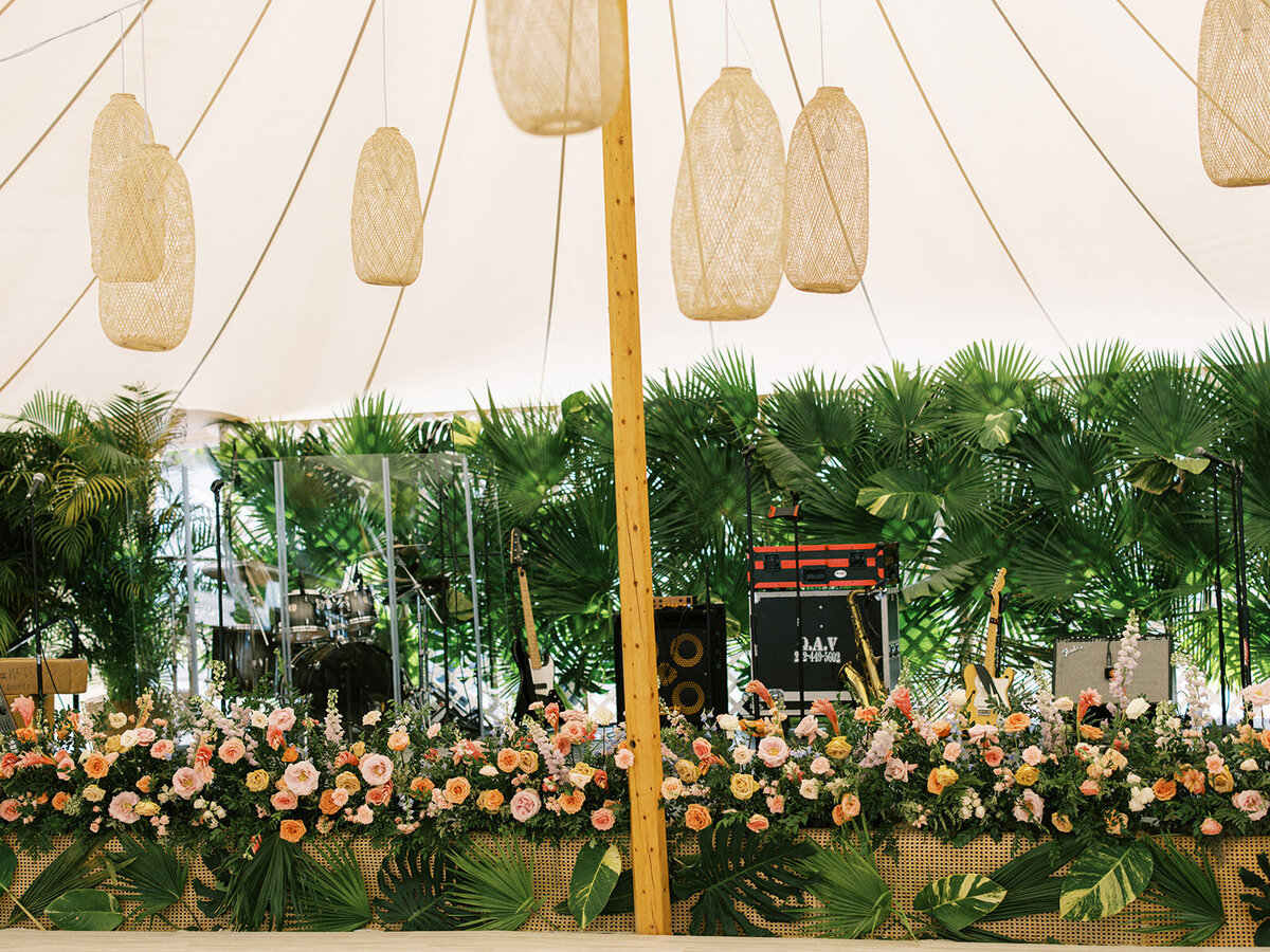 Floral stage façade and greenery backdrop for tropical beach wedding. Peach, pink, dusty blue, lavender, pale yellow, and cream color floral for private estate destination wedding in Exuma, Bahamas. Design by Rosemary & Finch Floral Design.