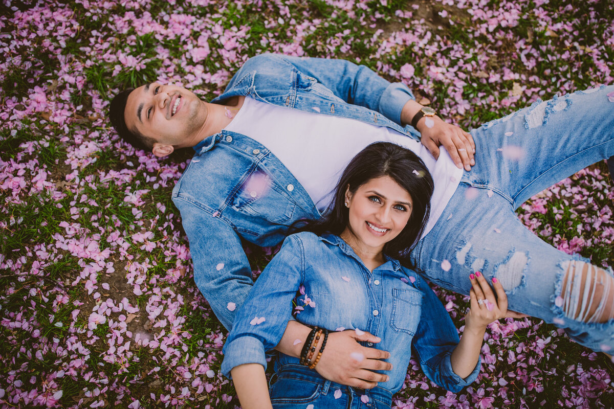 A couple in denim clothing laying down in a bed of cherry blossom petals