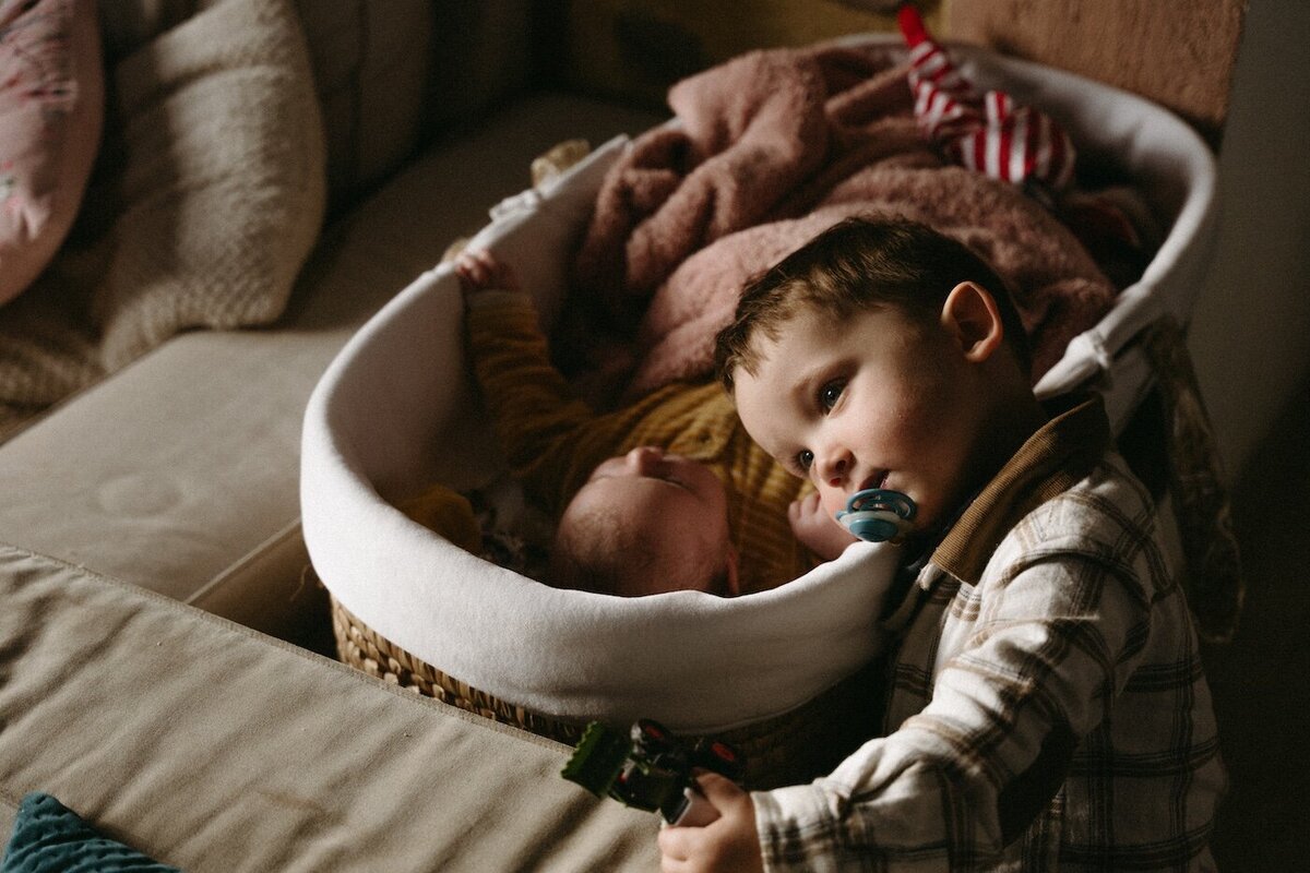 Grand frère veillant sur son petit frère endormi, instant de complicité et de douceur. Photographe Kamescop, séance photo naissance à domicile.