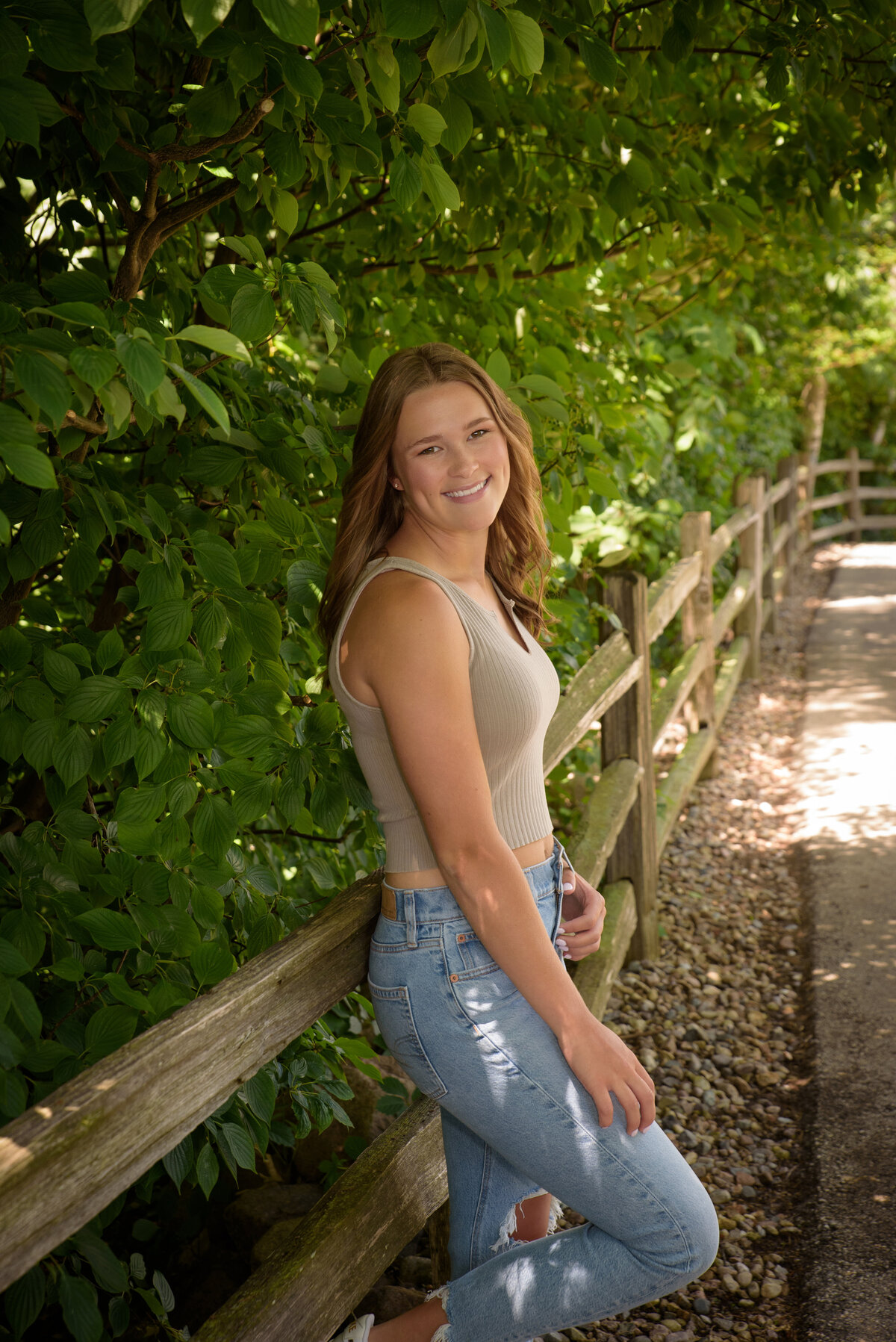 Luxemburg Casco High School senior girl wearing ripped jeans and a tan shirt standing along wooden fence at the Green Bay Botanical Gardens in Green Bay, Wisconsin