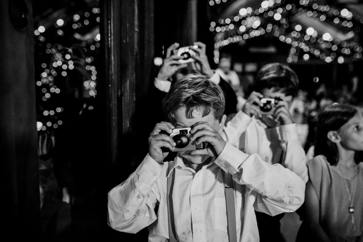 A group of people at a wedding reception taking pictures with disposable cameras.