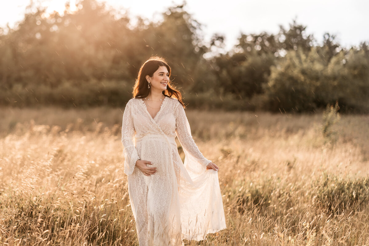 Photo of a pregnant woman standing in a field at sunset