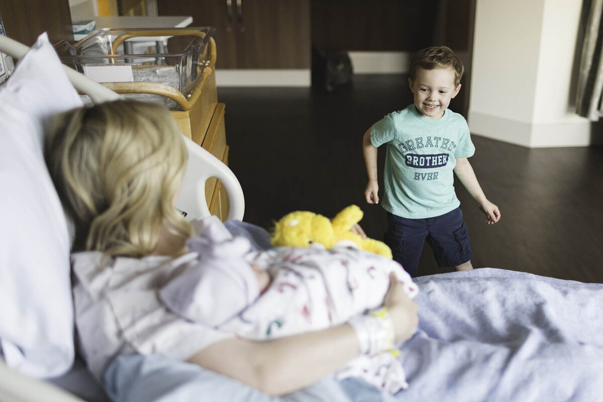 A big brother walks into a hospital room to meet his brand new baby sister who is in her mother's arms