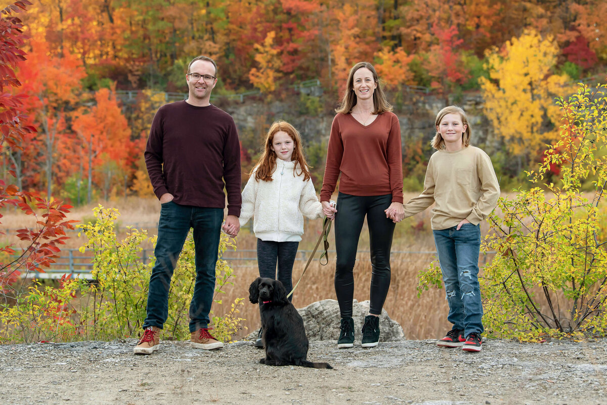 Mom and dad with their son and daughter holding hand in front of fall foliage for their Outdoor fall family photography session