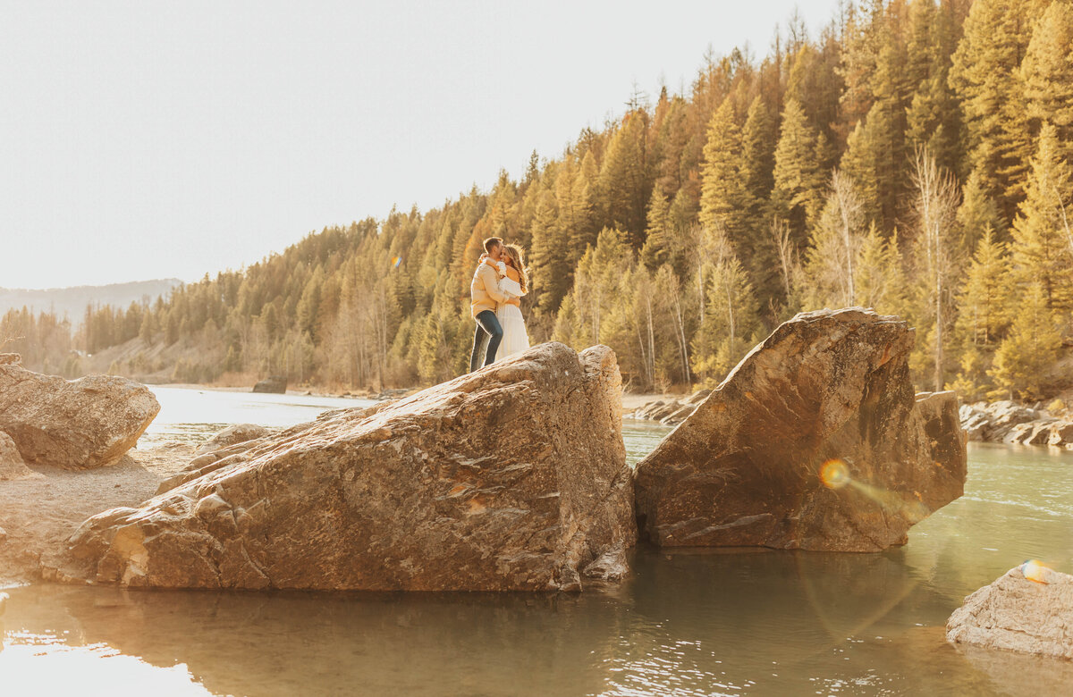 couple kissing on large rock in lake