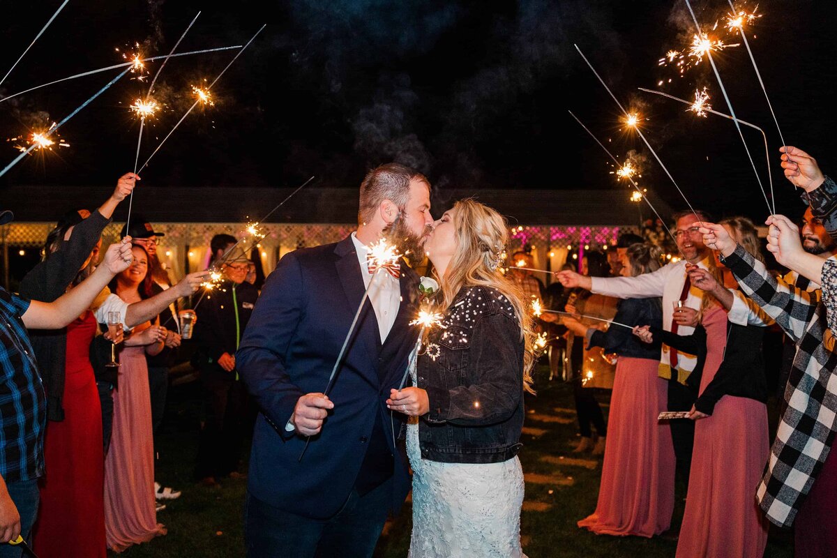 Bride and groom, kissing, in tunnel of friends, holding sparklers during wedding exit at Eagle Mountain Country Venue