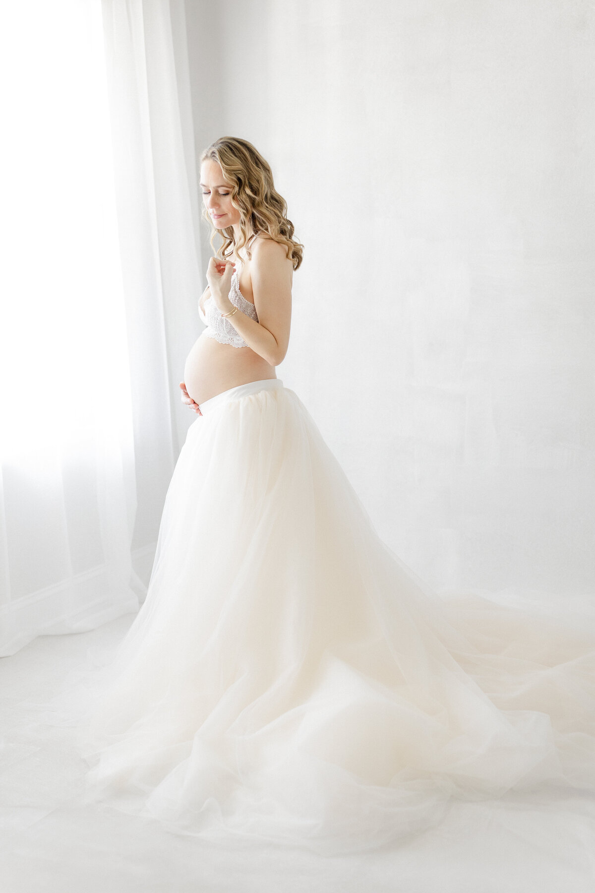 Graceful studio maternity portrait of Katie wearing a flowing tulle skirt, captured in natural light in Tampa