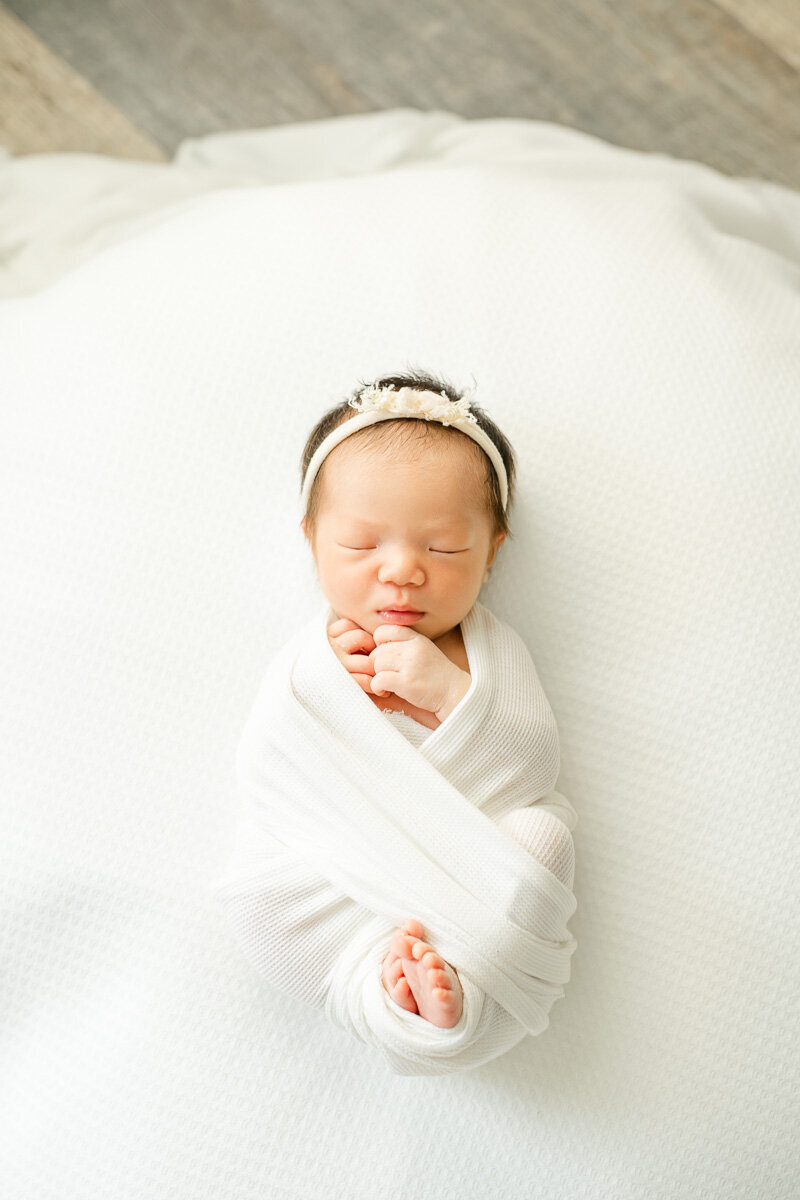 an infant baby girl lays on a white surface while sleeping during her newborn session with an Austin photographer.