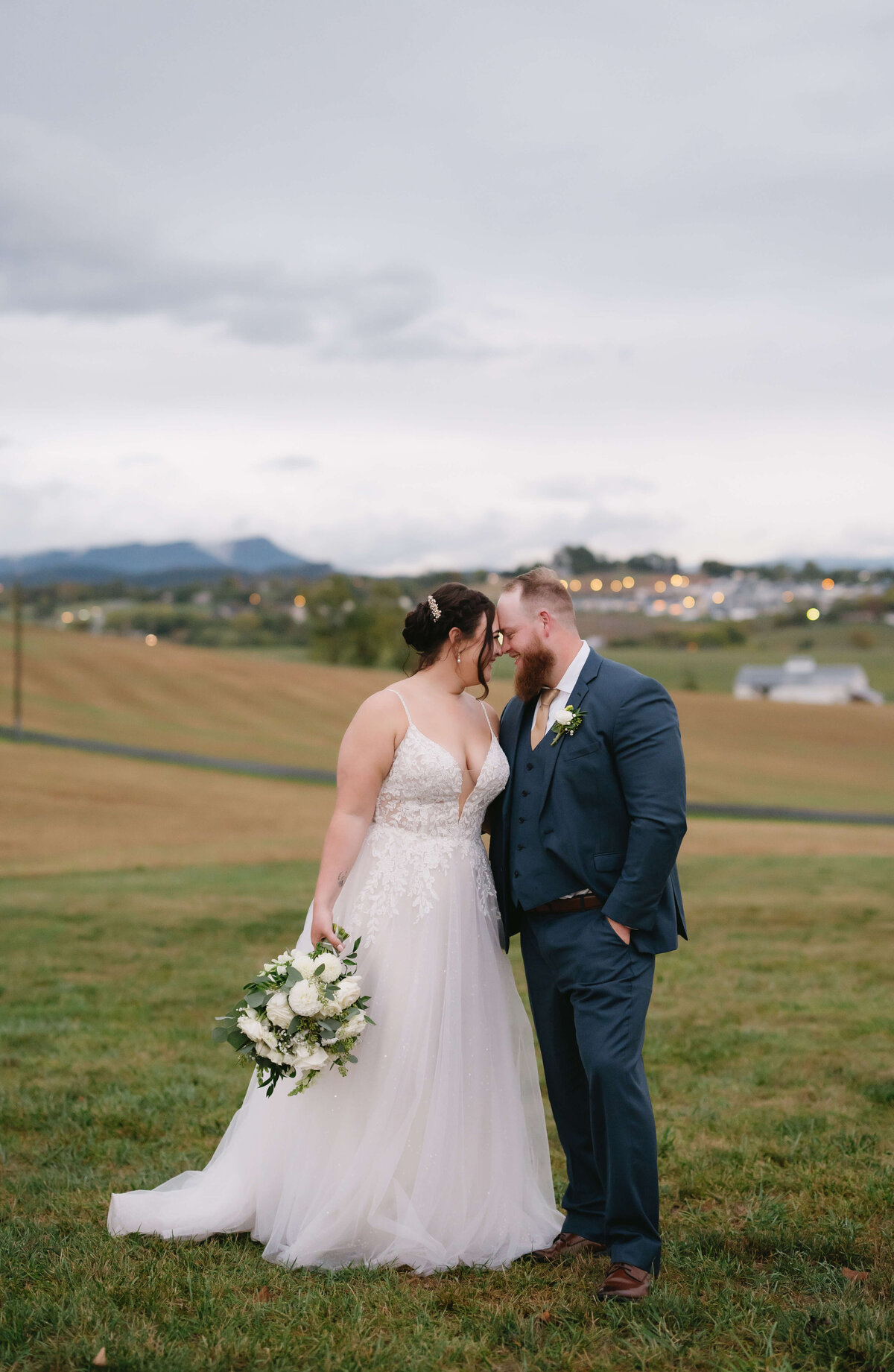 bride and groom standing close together and resting their foreheads together while standing on a hill with a city in the valley in the distance photographed by Charlottesville wedding photographer