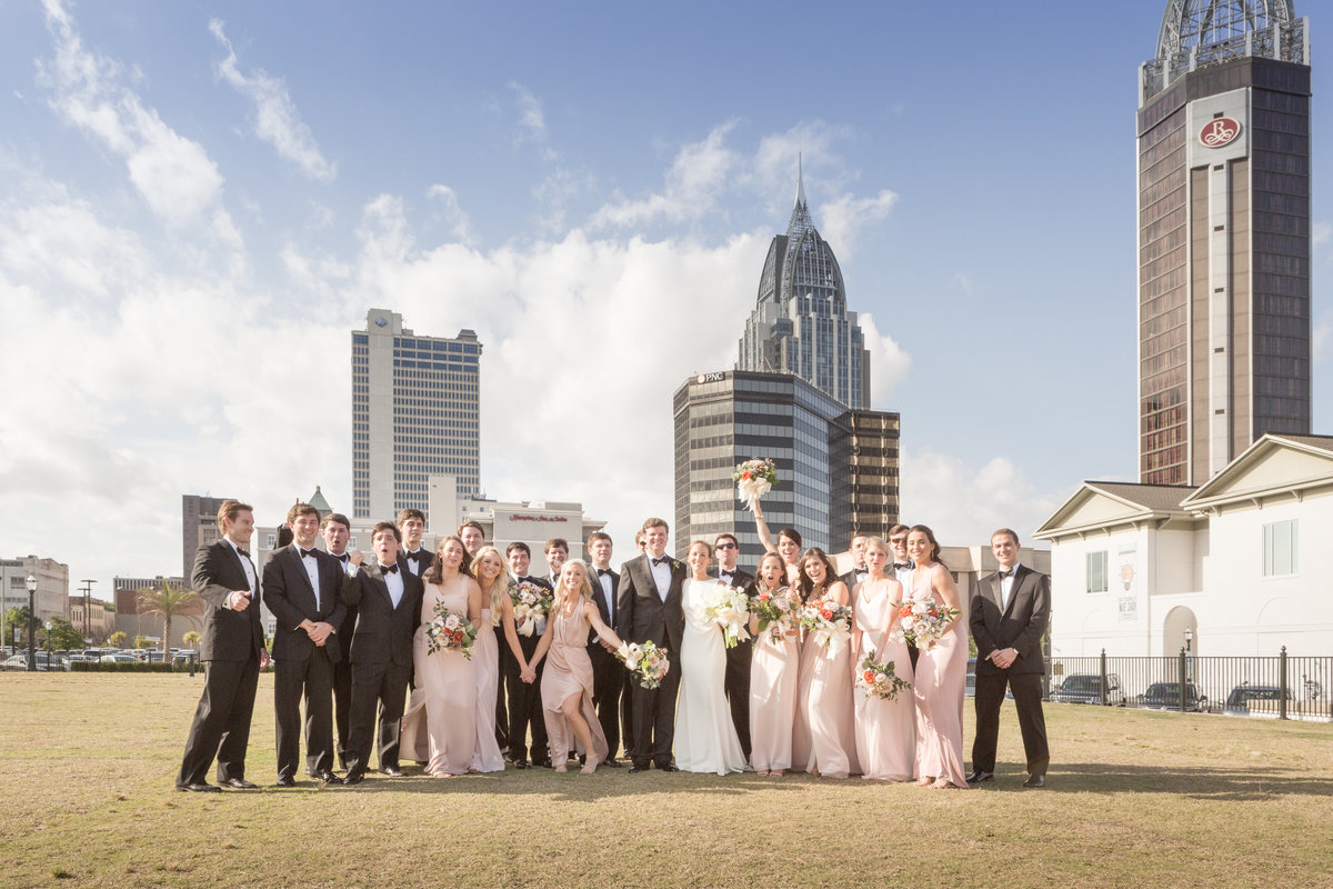 The entire wedding party celebrates the couple in this group photo with the skyline of Mobile, Alabama in the background.