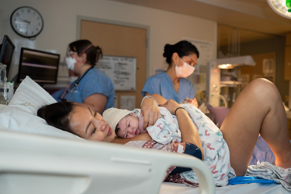 mother  laying in hospital bed holding baby after just giving birth at UW Medical Center in Seattle, WA.