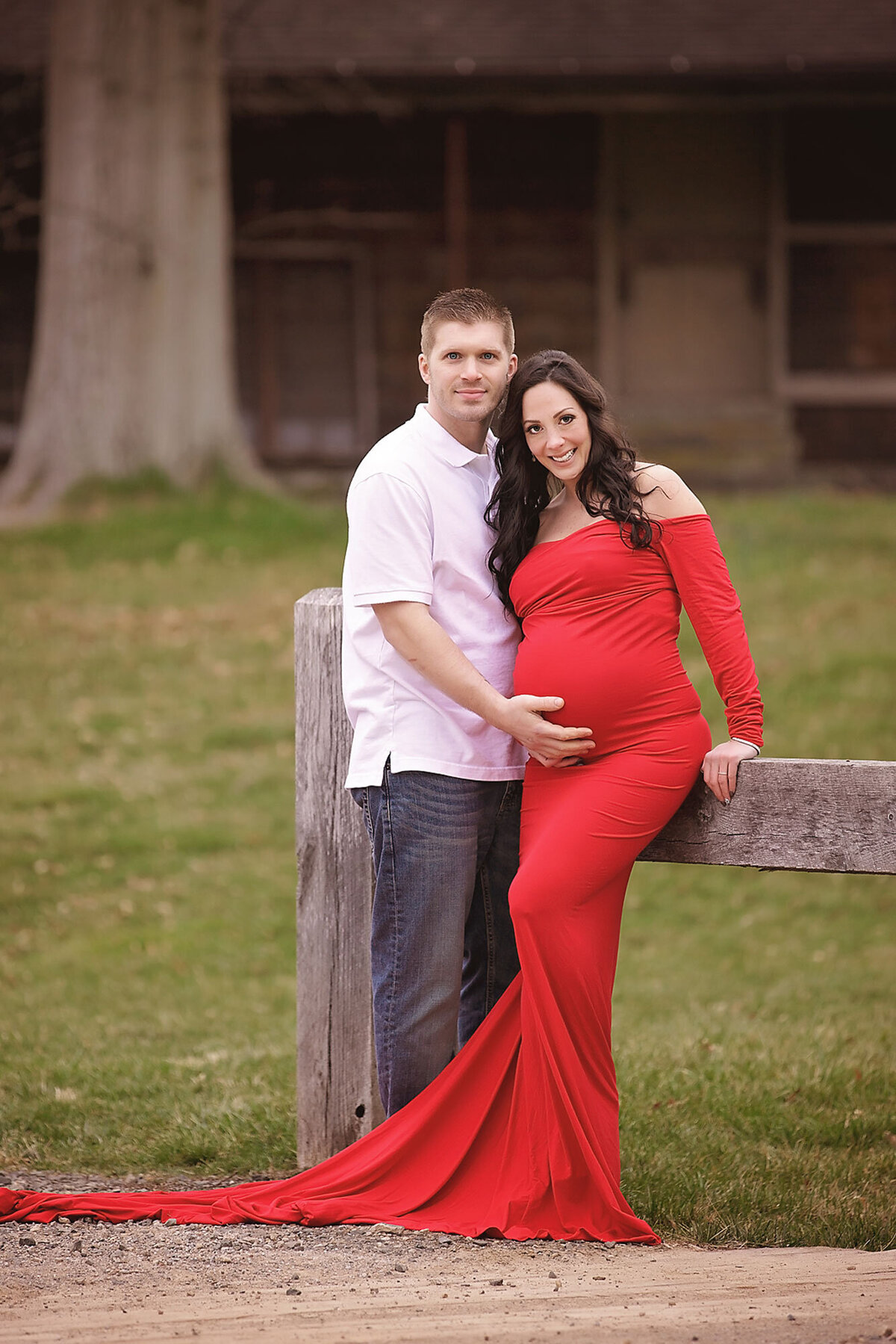 pregnant mom wearing a log red dress posing with her husband for maternity photo shoot