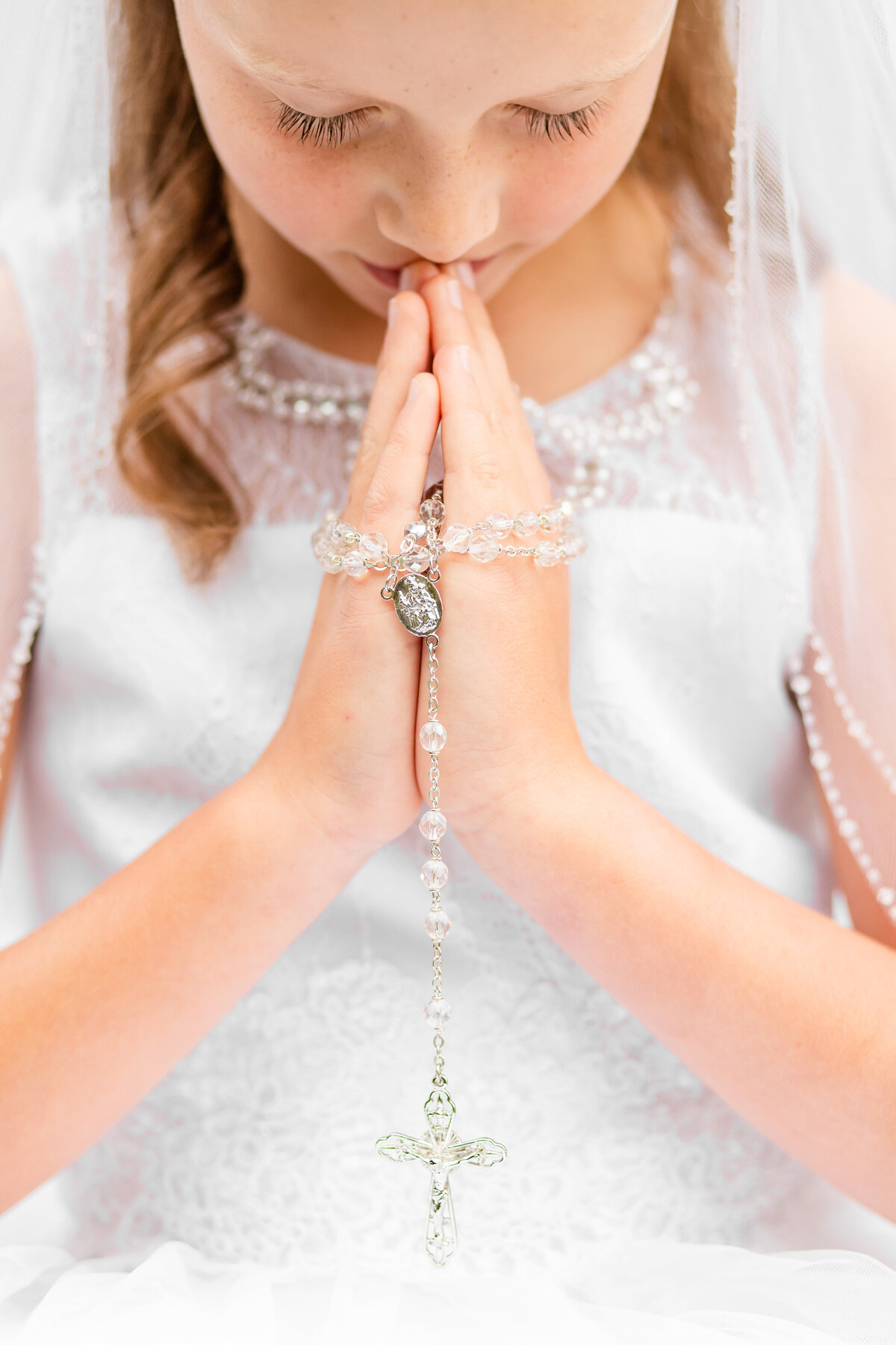 closeup of girl's first communion praying with rosary
