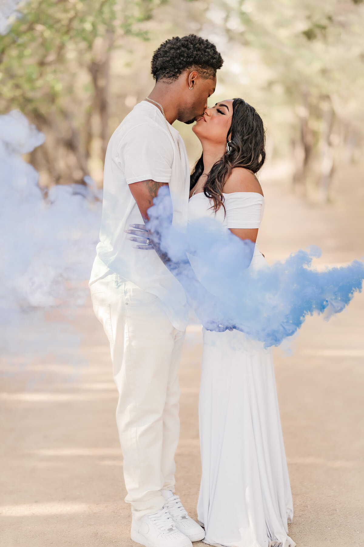 Couple kisses during San Antonio gender reveal pictures with blue smoke surrounding them.