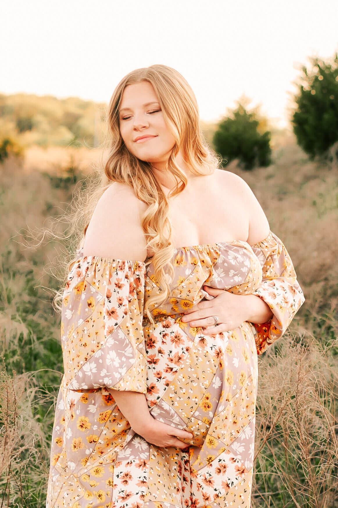 pregnant mom in floral dress hugging belly at a field in Springfield MO