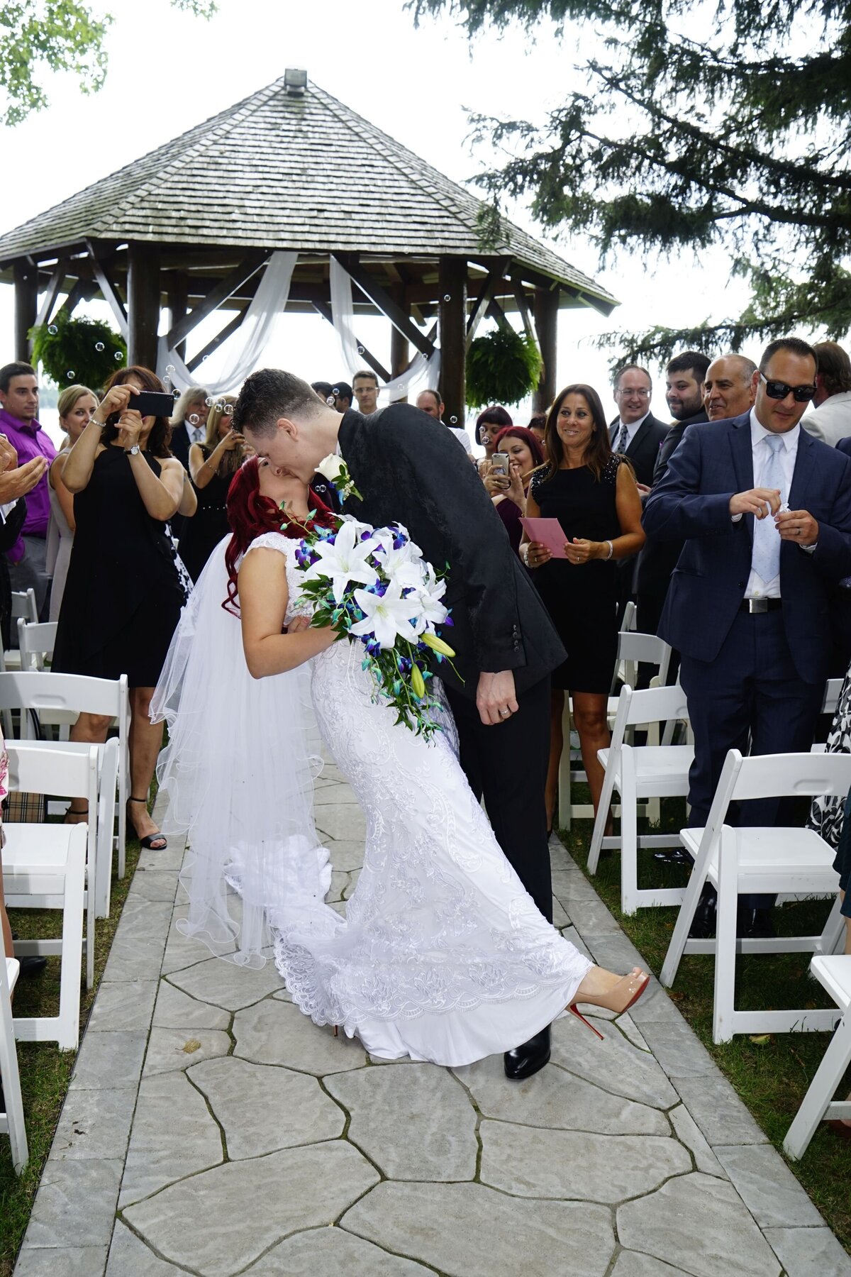 The groom dips the bride in a romantic gesture as they share a kiss in the aisle. This dynamic moment captures the excitement and passion of their wedding day, highlighting their playful and affectionate relationship.