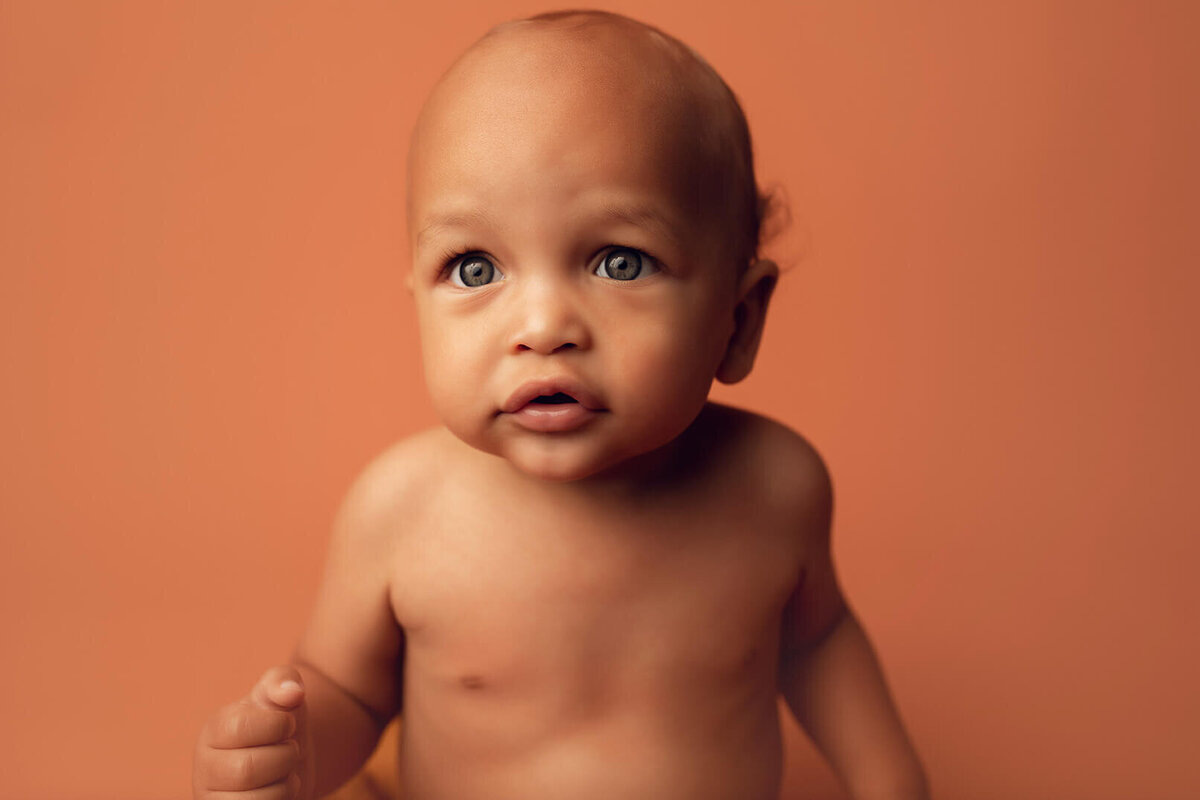 a close up of a one year old boy shirtless on a brown backdrop