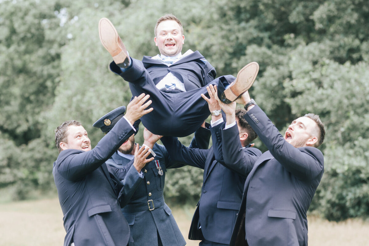 Groomsmen throwing the groom in the air and catching him