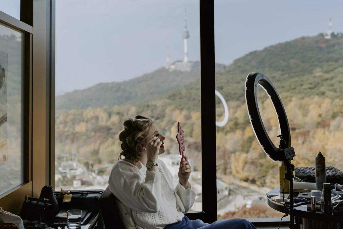 bride retouching her makeup in hotel showing the namsan tower