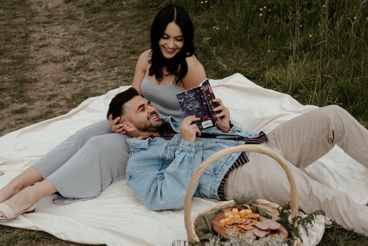 intimate picnic couples photos. The guy has his head in the girls lap and she is looking down at him while he reads a poetry book.