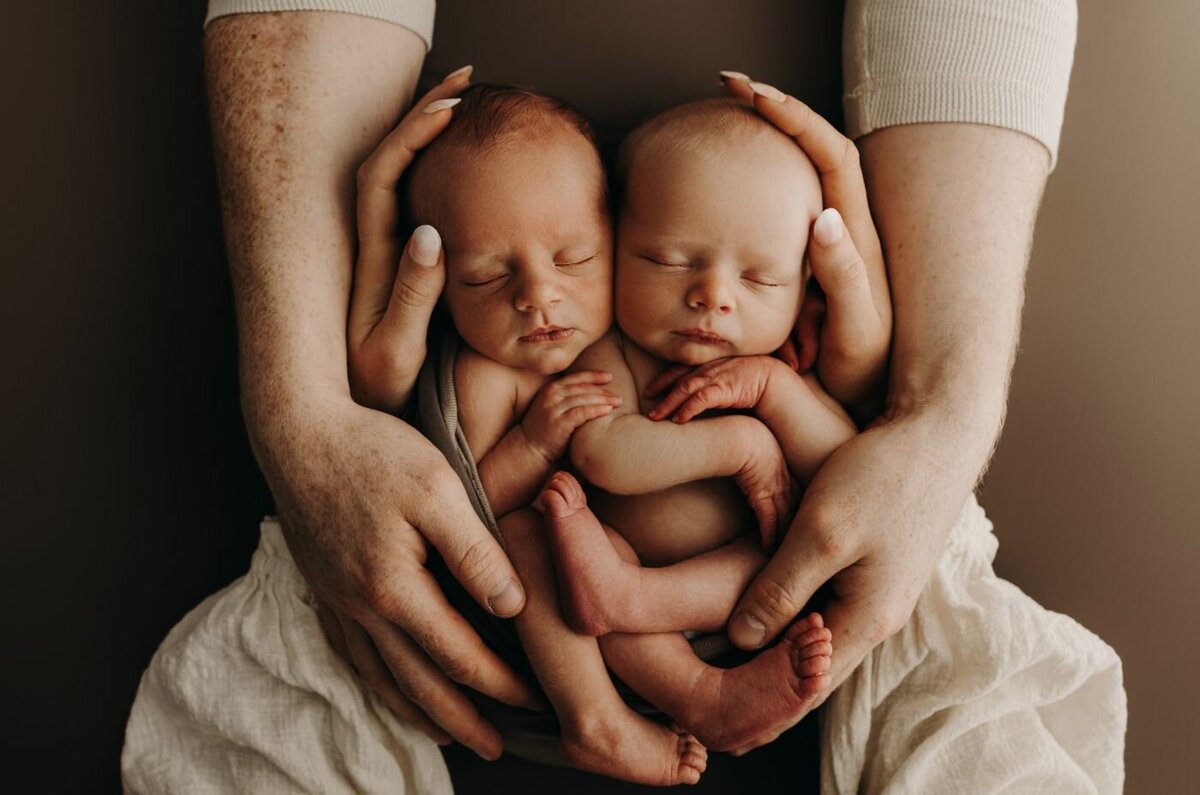 Sleeping newborn twins nestled in parent's hands during a tender photoshoot in Mullingar, Ireland
