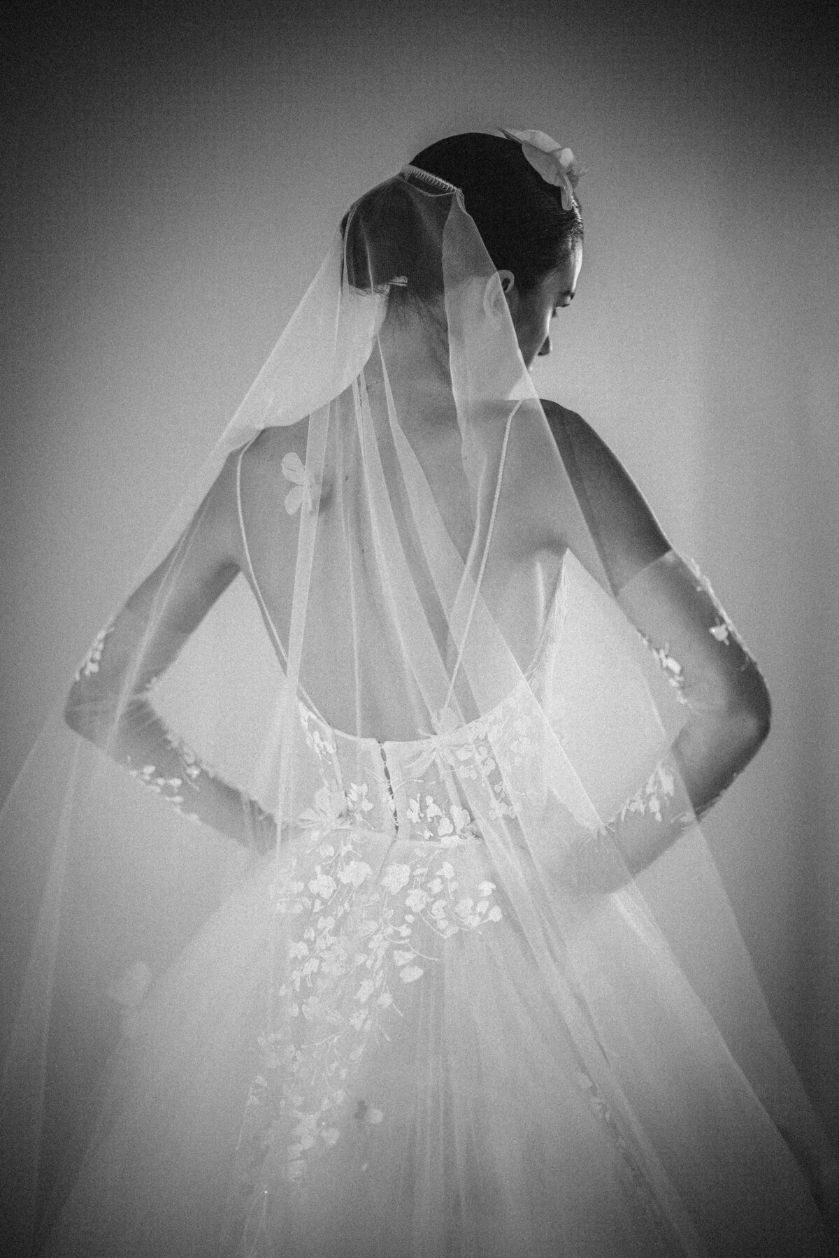 Black and white photo of a bride in a wedding dress with floral lace details, looking down, wearing a veil. This photo was taken by a Manhattan wedding photographer