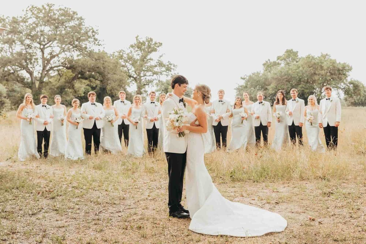 bride and groom hug while bridal party stands behind them