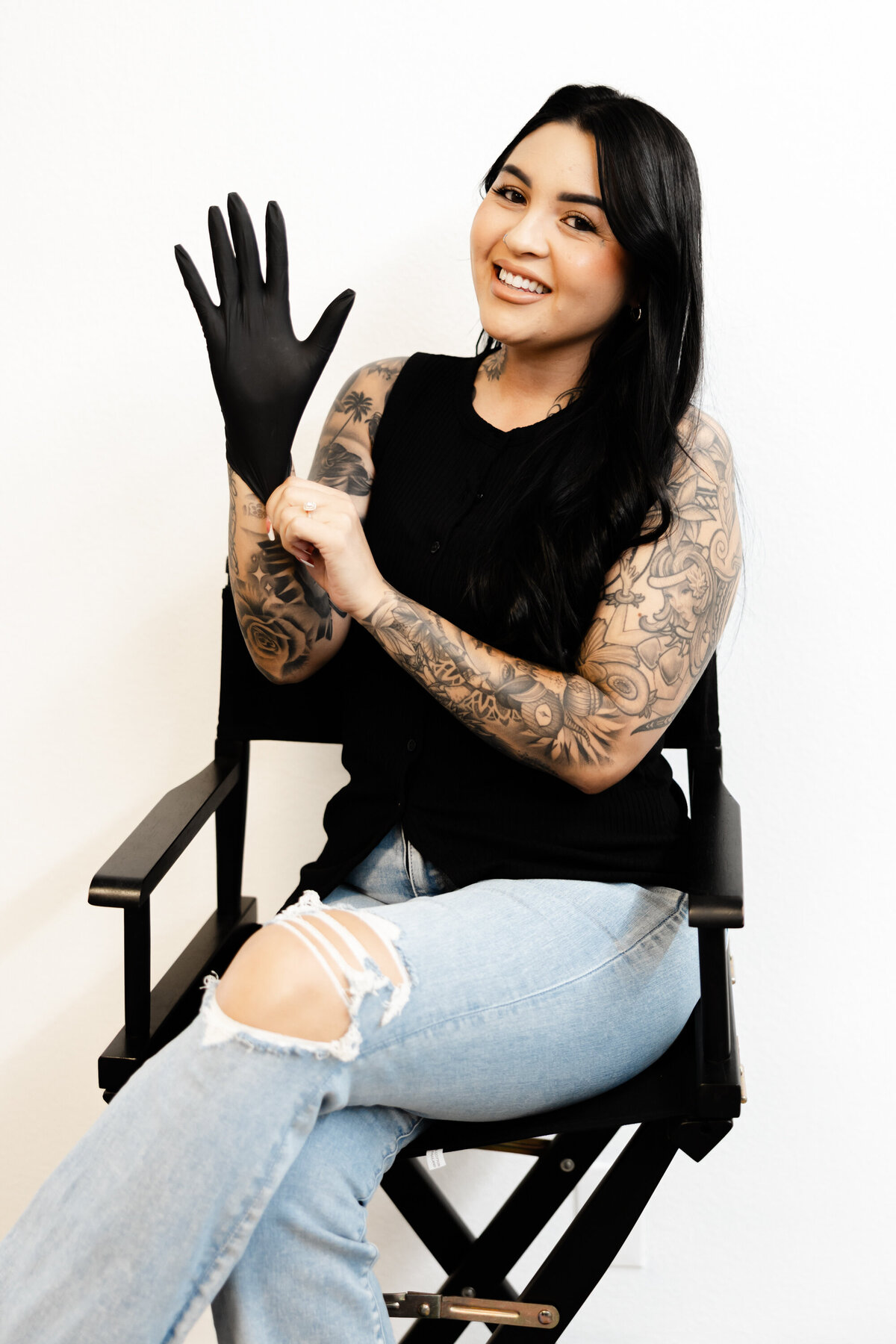Tattooed hairstylist smiling while putting on black gloves in a studio chair. Photograph by Yucaipa branding photographer Kaitlyn Dawn Photography.