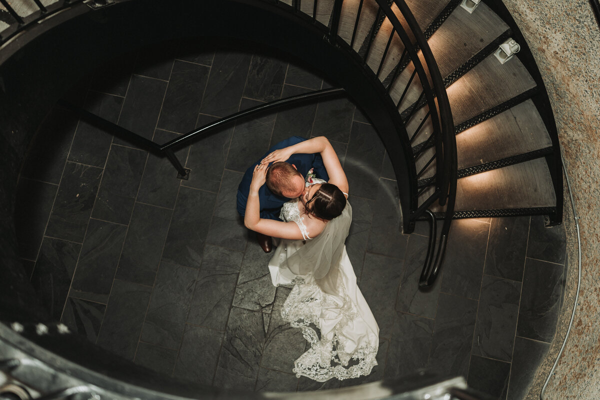 Aerial view of bride and groom sharing a romantic dance on a spiral staircase, with soft lighting highlighting the moment.
