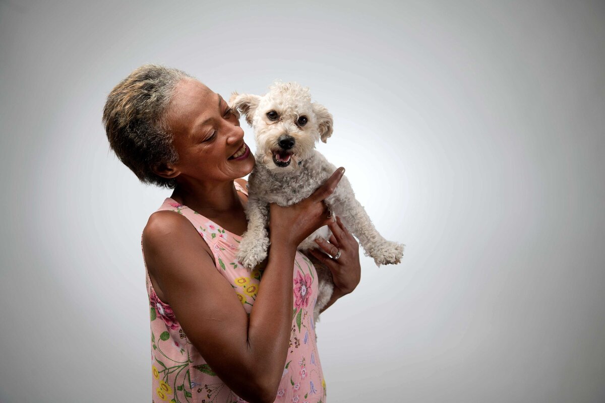A smiling women with her dog who is homeless is photographed in studio on a white backdrop for Father Joes Villages.