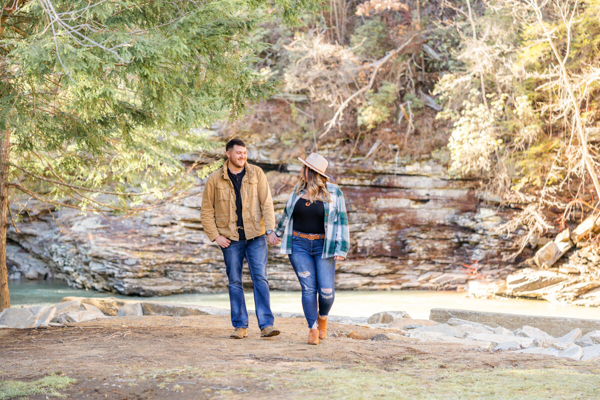 engaged man and women wearing cute hat walking hand in hand at the water's edge